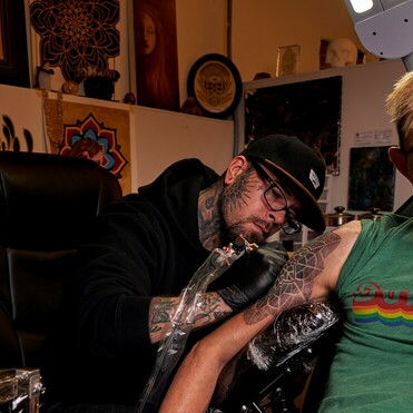 Photograph of tattoo artist Alan Lott working on a mandala dot bicep tattoo at Sacred Mandala Studio in Durham, NC.