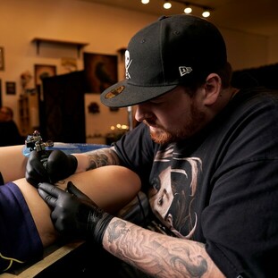 Photograph of Ray Durham working on an upper leg tattoo at Sacred Mandala Studio in Durham, NC